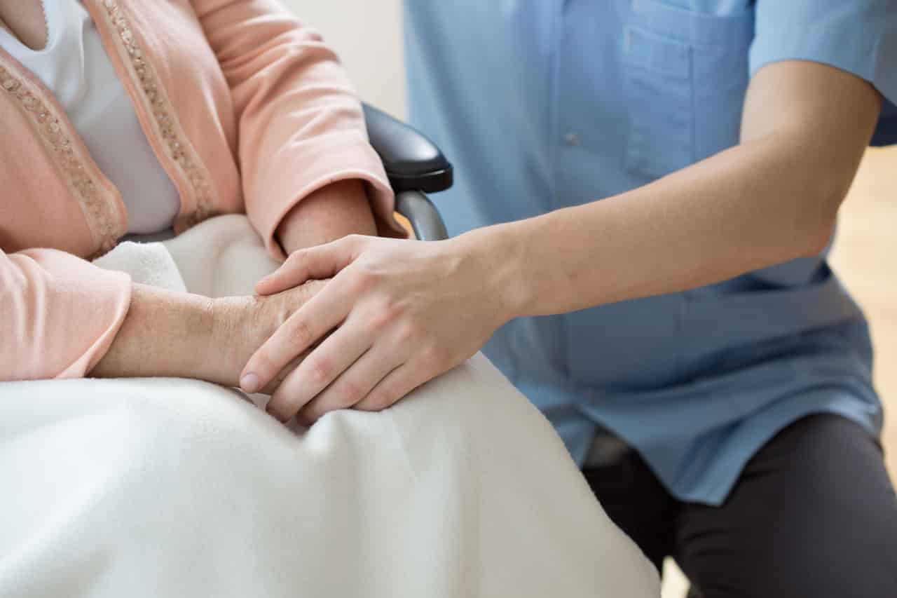 Eine Altenpflegerin hält die Hand einer alten Frau